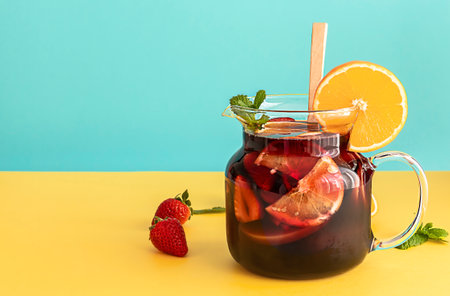 Summer cold cocktail, fruit and berry red wine sangria with apple, lemon, oranges, and strawberry. blue and yellow background, copy space.の写真素材