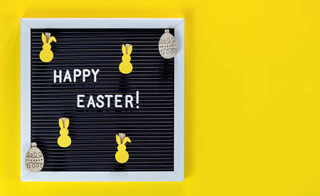 HAPPY EASTER is written on letter board and wooden decorations on yellow background. Copy space, top view. Flat lay of Easter celebration concept.の写真素材