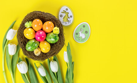 Easter eggs in the nest and wooden decorative bunny on yellow background. Holiday concept, copy...