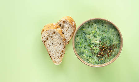 Healthy food delivery concept. Fresh broccoli cream soup served fresh bread and spices in craft container on green background. Vegetarian lunch to go.の写真素材