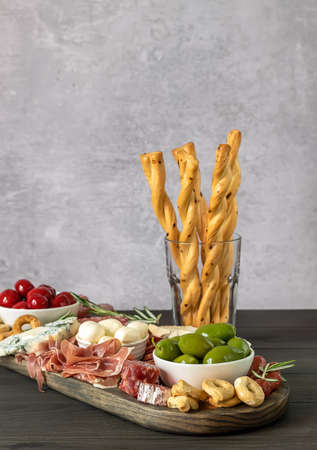 Appetizers board with different italian antipasti, cheese, charcuterie, olives, and crackers over wooden table. Vertical orientation, selective focusの写真素材