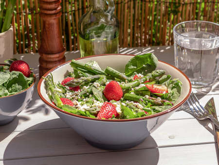 Fresh strawberry, green asparagus, feta cheese, baby spinach, and arugula salad served in a bowl with sparkling water. natural summer light and trendy strong reflection. Selective Focus.の写真素材