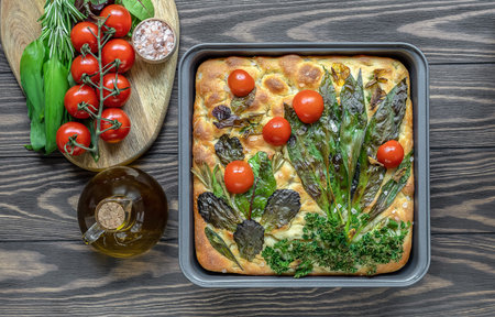Homemade baked flower focaccia bread art with herbs and vegetables. Seasonal wild garlic leaves. Top view, wooden table.の写真素材
