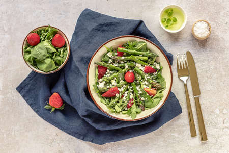 Delicious healthy salad of fresh strawberries, green asparagus, feta cheese, arugula, lettuce. Clean eating, lunch bowl. Top view.の写真素材