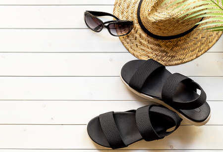 Womens open-toe black sandals from recycled plastic fibers, straw hat, sunglasses on the wooden boardwalk. Summer traveling concept.の写真素材