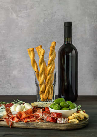Appetizers board with different italian antipasti, cheese, charcuterie, snacks and wine over wooden table. Vertical orientation, selective focusの写真素材