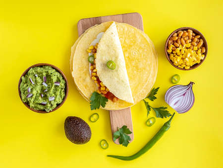 Tortilla wrap or burrito with corn, beans, greens, and homemade guacamole. Vegetarian healthy food, yellow background.の写真素材