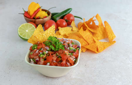 Mexican appetizer Pico de Gallo in a bowl and ingredients on the table. Homemade salsa sauce, great dip for nachos chips. Selective focus.の写真素材