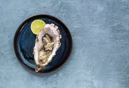 Fresh opened big Oyster close-up on blue plate, with lemon. Healthy gourmet seafood. Copy space,...