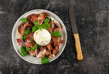 Salad with Tomatoes, Prosciutto, and Burrata cheese with basil and olive oil. Italian appetizer. Flat lay, copy space.の写真素材