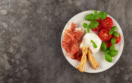Salad with Tomatoes, Prosciutto, and Burrata cheese with basil and olive oil. Italian appetizer. Flat lay, copy space.の写真素材