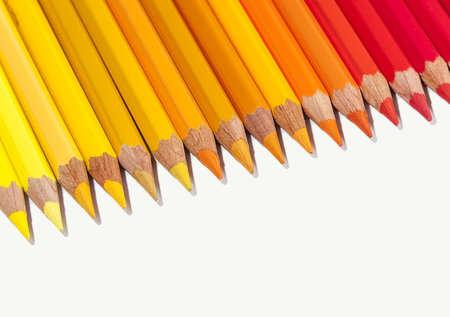 Isolated color pencils in line on white background as a border with copy space. Mostly red, orange and yellow.の写真素材
