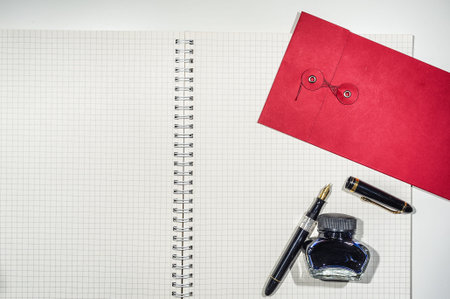 Workspace with open notebook, classic pen, blue ink and red envelope