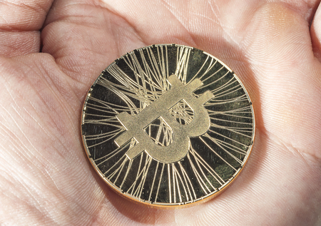 Shining gold metal BTC bitcoin coin lying on human hand.の写真素材