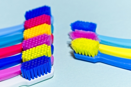 Used and new colorful professional soft toothbrushes with lot of bristles in straight cut in oppositing lines on light blue background.の写真素材