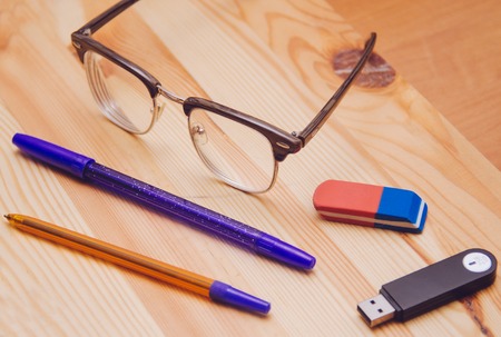 Glasses in clubmaster frame, flash usb card and pens on the wood tableの写真素材