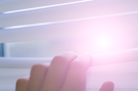 Male hand separating slats of venetian blinds with a finger to see through with soft lightの写真素材