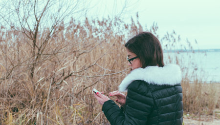 Girl using a smart phone on the beach of lake in autumn time