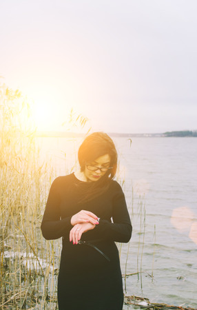 Woman checking the time on the lake in sunset timeの写真素材