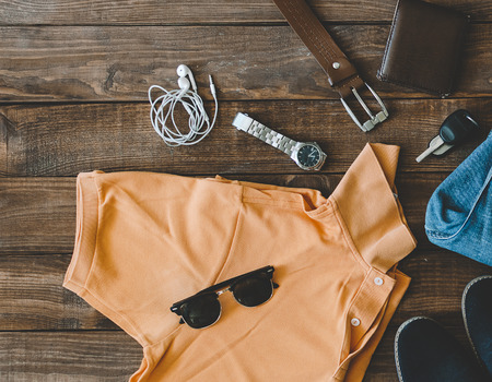 cool fashion men's casual outfit on wooden table, trendy in summer, t-shirt polo, shues, blue jeans pants, sunglasses, watch, wallet and belt, top viewの写真素材
