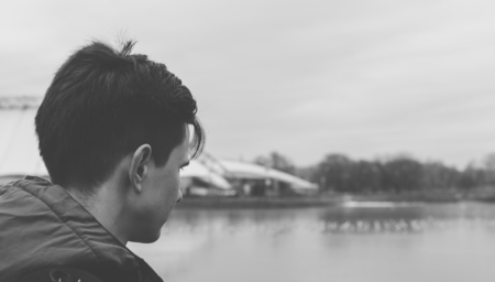 Black and white photo of the young man standing on the bridge and looking into the distance on the riverの写真素材