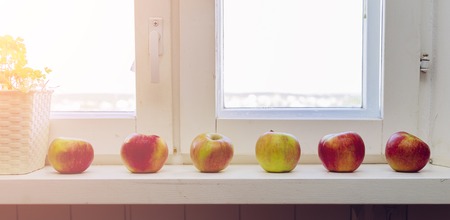 White wooden windows pane with apples and plant with outside view of beautiful sun in sunset or sunrise timeの写真素材