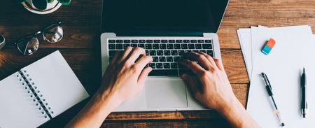 A man is working by using a laptop computer on vintage wooden table. Hands typing on a keyboard. Top...
