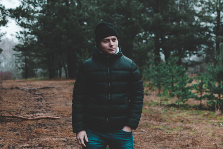 Handsome young man in winter clothes with a backpack on the background of an autumn forest.の写真素材