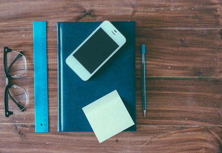 Glasses, pen, notebook and phone on wooden tableの写真素材