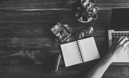 Black and white photo of the man is typing on a laptop on messy wood office table.の写真素材