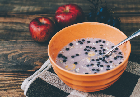 Yogurt with granola, grapes and fresh apples, in orange bowl over old wood background. Vintage effect.の写真素材