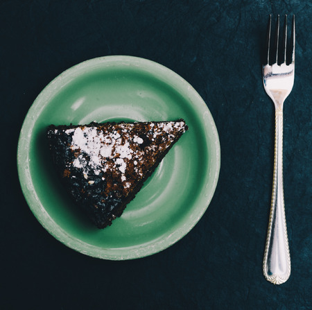 Chocolate cake on green plate and fork on the black backgroundの写真素材