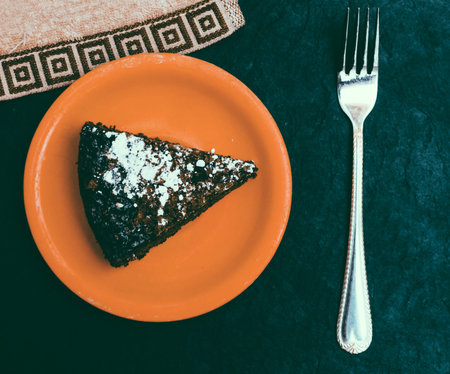 Chocolate cake on the orange plate and fork on the black background