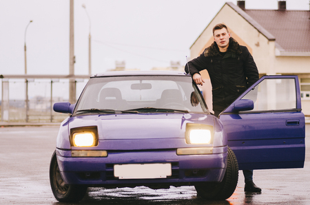 Young man with old car on city streetの写真素材