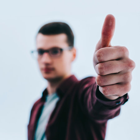 Smiling young man with glasses on blue background wall with thumb up