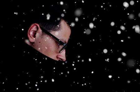 Man in coat on black background with snowfallの写真素材