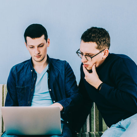 two young men working with laptop sitting on sofa