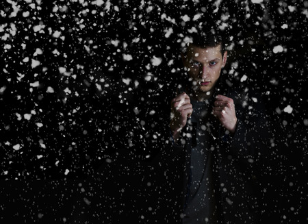 Man in coat on black background with snowfallの写真素材