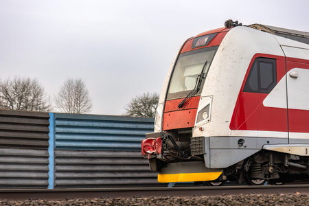 The front part of a passenger train moving along the noise barrier.