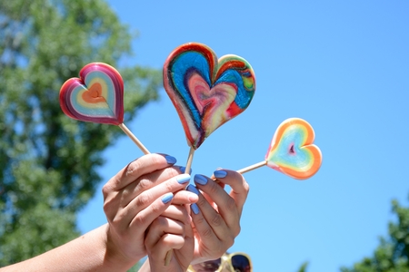 Three lollipops in woman's and kid's hands against blue sky and trees.の写真素材
