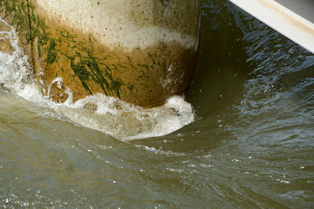 Water flow around concrete round wall corner in river.の写真素材