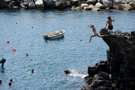 Manarola, Italy - September 4, 2016: Unidentified woman jumping from high rock to sea in Manarola city in Liguria, Italy.  One of five Cinque Terre cities (unesco world heritage). Unidentified people visible.のeditorial素材