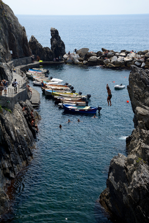 Manarola, Italy - September 4, 2016: Unidentified woman jumping from high rock to sea in Manarola city in Liguria, Italy.  One of five Cinque Terre cities (unesco world heritage). Unidentified people visible.のeditorial素材