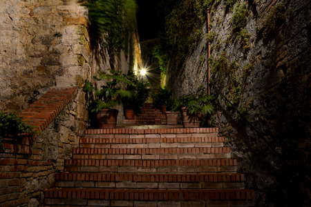 Narrow passage and stairs at night in San Gimignano in Tuscany, Italy. Blurred plants in pots moved by windの写真素材
