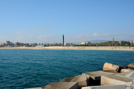 Barcelona, Spain - December 3, 2016: Stones, sea, beach and buildings in Barcelona, Spain. Unidentified people visible.のeditorial素材