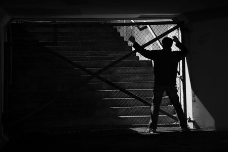 Man silhouette desperately trying to escape from the locked metal woven wire gate  の写真素材