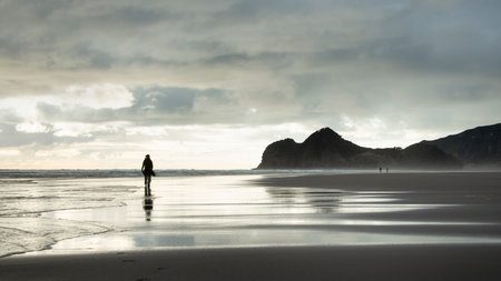 Silhouette image of people walking on Bethells beach, Waitakere, Auckland