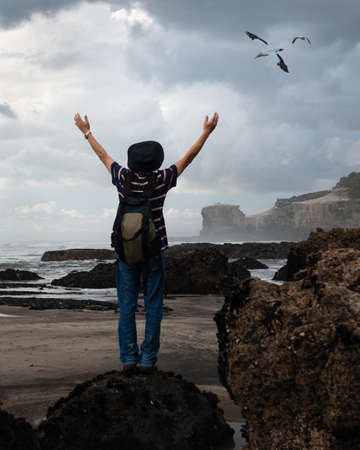 A man raising his hands towards the flying gannets at Muriwai beach, West Auckland. Vertical format.の写真素材
