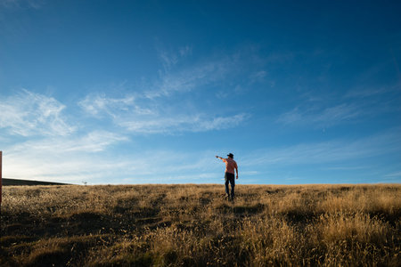 Tourist standing on the dried yellow grass and pointing at the sun, moments before sunset with a...