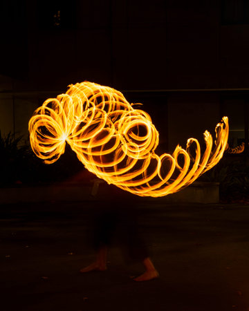 Street artist juggling with burning poi at fire performance. Long exposure image of abstract fire...